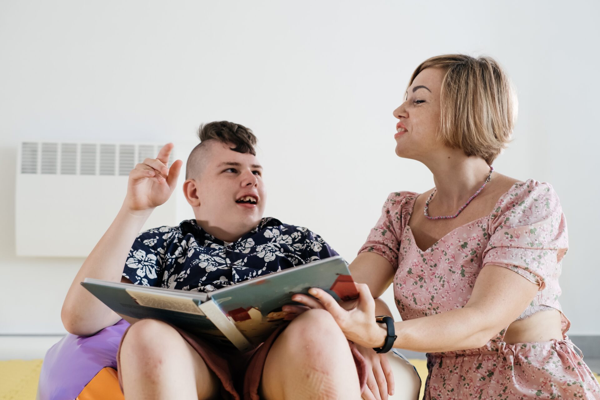 Children with disability reading book and communicating. Cerebral palsy boy talking with woman tale therapist. Rehabilitation center, mother with teenage person learning to speak, pronounce at home