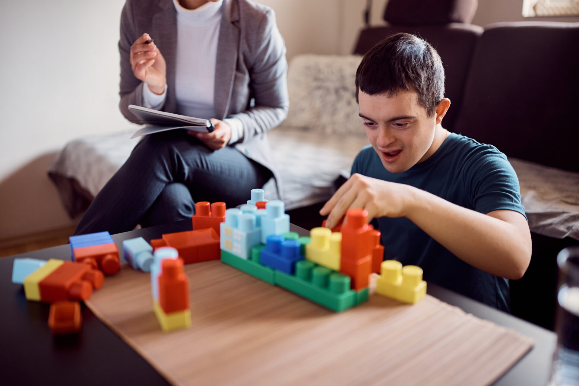 Happy down syndrome man playing with toy blocks and having fun with psychologist during home visit.