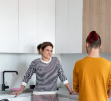 A disabled mature woman in wheelchair talking to son in kitchen indoors at home.